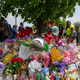 People walk by a memorial for the victims of the Buffalo supermarket shooting outside the Tops Friendly Market on Saturday, May 21, 2022, in Buffalo, N.Y. Tops was encouraging people to join its stores in a moment of silence to honor the shooting victims Saturday at 2:30 p.m., the approximate time of the attack a week earlier. Buffalo Mayor Byron Brown also called for 123 seconds of silence from 2:28 p.m. to 2:31 p.m., followed by the ringing of church bells 13 times throughout the city to honor the 10 people killed and three wounded.